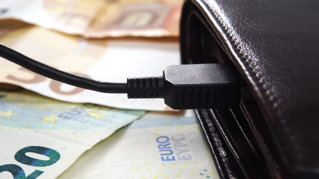 USB charger with a black electric cable connected to a brown leather wallet on euro banknotes. Macro. Money and wealth charging concept. Dolly Shot