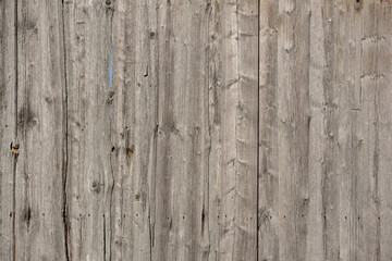 The background and texture of a wall made of old faded wood partially showing the blue sky, outdoors
