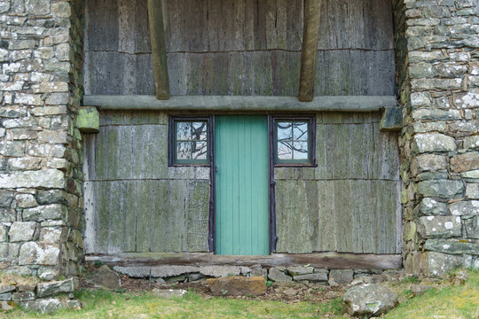 Teal door and small square windows on an unusual old wood and stone building