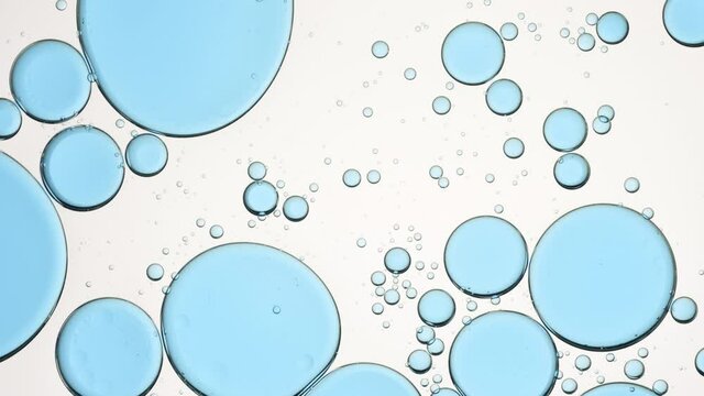 Blue different sized clear bubbles move slowly and spontaneously in transparent liquid against white background | Background for moisturizer advertisement shot