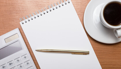 On a light wooden background, a white cup of coffee, a white calculator, a golden pen and a blank notebook with a place to insert text. Template. Business concept