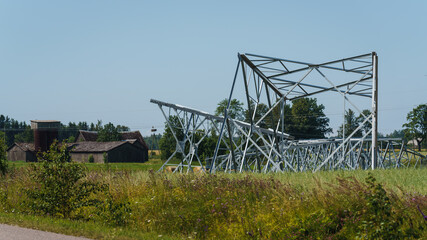 the iron structures of the power line lie in the meadow before installation, old wooden buildings can be seen below