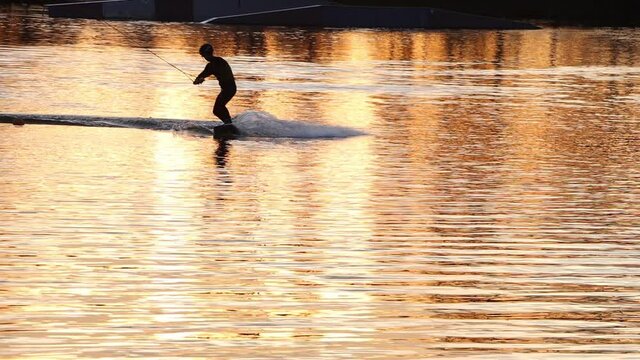 Silhouette of an athlete riding a water ski at sunset