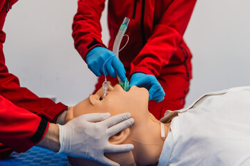 Side view of two paramedics in red uniforms on training for endotracheal intubation using medical dummy. Close - up
