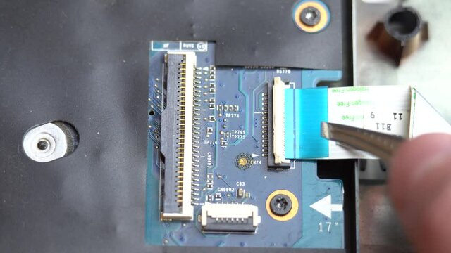 Connecting a flex cable to the laptop motherboard with tweezers, laptop repair in a service center