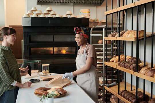 African young woman packing fresh bread and selling it to the customer in bakery shop