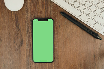Green Chroma Key on smartphone screen on wooden background with a computer beside it.