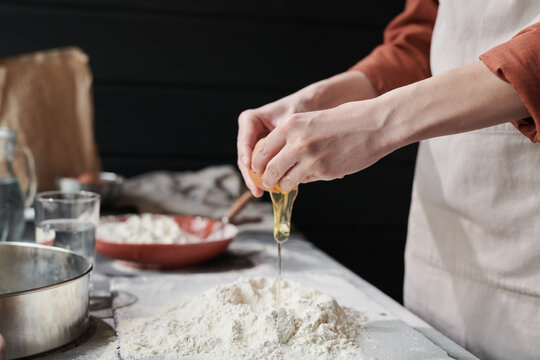 Close-up of woman adding egga and making a dough while baking the pie in the kitchen