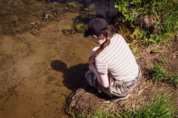 The girl squats by the lake and looks at the water.