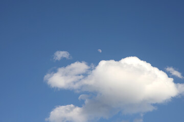 daytime moon in a blue sky with fluffy clouds