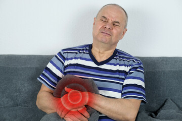 adult bald man sits on a sofa, holds his hand on the right side of the hypochondrium, a grimace of...