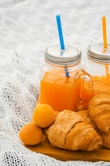 Orange juice in glass jars and fruit with croissants. 