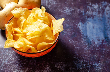 Still life of a bowl of potato chips with raw potatoes and a linen cloth.