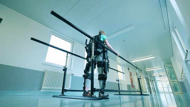 Young woman is practicing walking in the exoskeleton in hospital