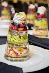 3 piece food tower containing layers of grilled chicken salad and fruit parfait with flavoring drip. Side view with more towers in the background