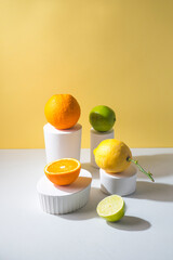 Citrus fruits conceptual creative  still life  in white stands and podiums in the yellow background and hard shadows, pop-art style. Healthy food concept
