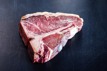 Dry aged and raw T bone steak isolated on a black cutting board