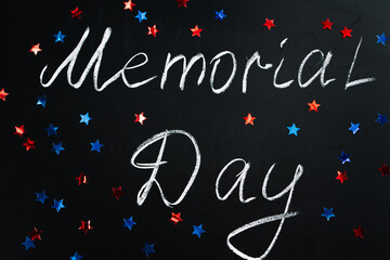 Handwritten inscription Memorial Day on a black chalkboard and American blue and red stars on background. Holiday concept.