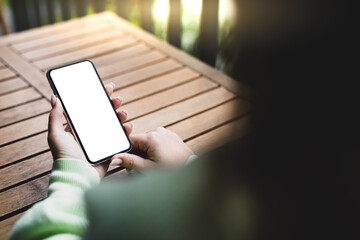 Girl holding a smartphone with a blank screen on the background of a wooden table in the garden. View from behind the shoulder.