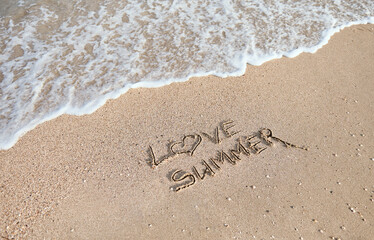 Handwritten inscription, letters, I Love Summer on the wet sand on the background of the sea wave washing away with water.