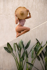 Beautiful woman with perfect legs in red bikini posing near the wall with big hat