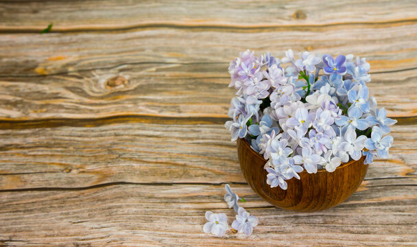 Beautiful inflorescences of lilacs in a wooden cup on a wooden background. Image with selective focus