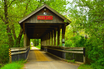 Fototapeta na wymiar Covered wooden foot bridge over small peaceful creek in Reed City, Michigan.