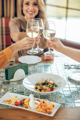 Smiling young woman holding a glass of wine and toasting with friends