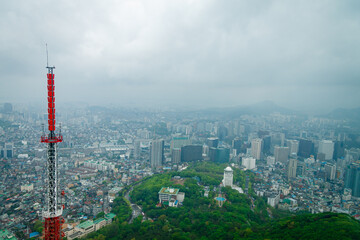 Cityscape with TV (Television), radio tower on mountain hill, green tree and city in the background with cloudy sky.