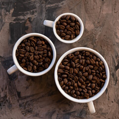 Three Cups are filled with roasted coffee beans. Flat Lay. White cups different sizes, from smallest to largest, on vintage blurred background. Soft focus.