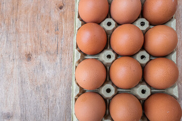 Twelve fresh eggs in a box, on a wooden board.