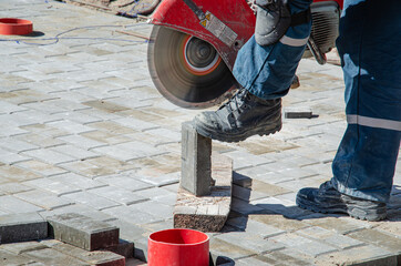 A worker cuts paving slabs with a gas cutter and a hand saw