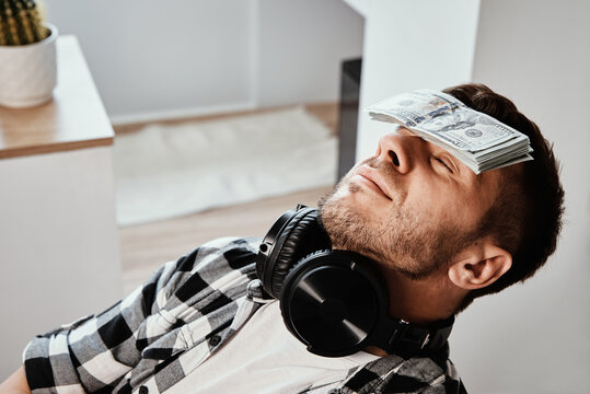 Man sleeping in workplace with stack of dollar bills on his forehead
