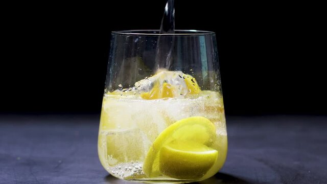 Pouring soda in glass with sliced lemon and ice cubes