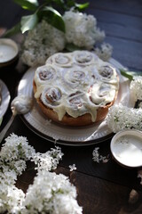 Cinnamon rolls covered with butter cream on a table with white lilacs. Breakfast with rolls and milk.