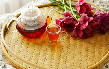 Fototapeta na wymiar on a rattan round tray, there is a cup, a teapot, and tulips. the concept of breakfast in bed