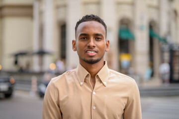 Naklejka premium Portrait of handsome black young African businessman smiling outdoors in city