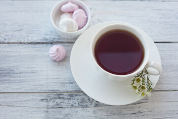 White cup with tea on a white wooden background with sweets.