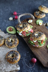 Bagels with salmon, avocado and green lettuce on a wooden board. Breakfast with light healthy snacks.