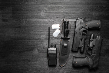 Black airsoft gun, walkie talkie radio station and knife and soldier badge on the black flat lay background with copy space.