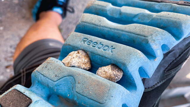 Reebokのスニーカーの靴底、ライトブルーのソールに挟まった石ころ。運動、アクテビティ、ワークアウトの1コマ