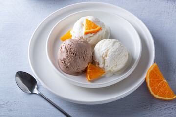 Vanilla and chocolate ice cream and orange slices in a plate on a light wooden table
