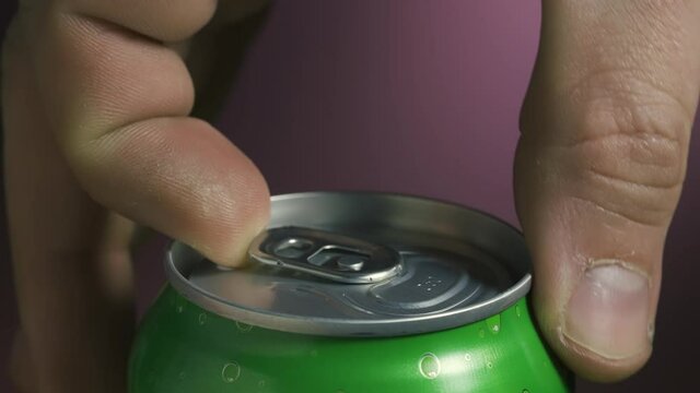 A man opens a green can of beer on a blurred background. A white frothy fountain pours from a shaken jar. Beer in a metal jar. Slow motion. Close up.