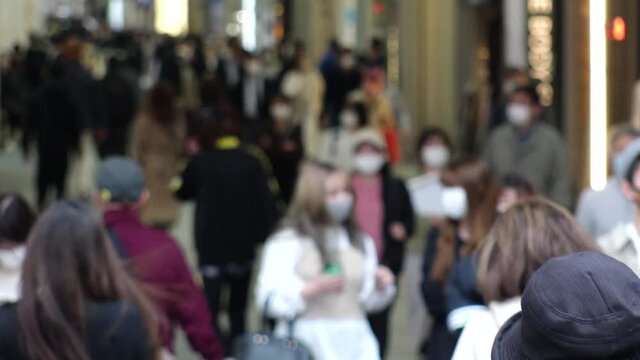 OSAKA, JAPAN - APRIL 2021 : Crowd of people wearing surgical masks to protect from Coronavirus (COVID-19) at Namba, Shinsaibashi shopping street. Slow motion shot.