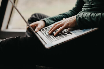 Mans hands with a laptop at an unusual window.