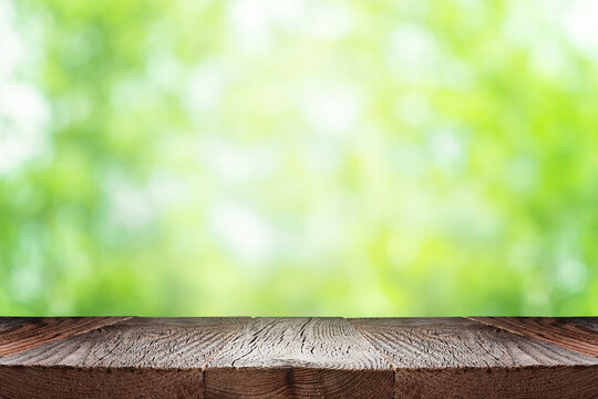Empty wooden table or board over green blurred nature background. Summer background with empty space for product display
