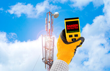 Measuring electromagnetic radiation from a cell tower. The device indicates hazardous radiation with text Danger. Influence of the electromagnetic field on humans concept. - obrazy, fototapety, plakaty