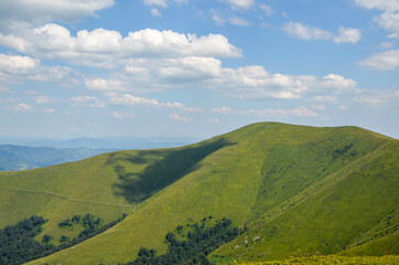 Fototapeta na wymiar Blue sky with fluffy clouds over the Borzhava mountain ridge with grassy hillside. Gorgeous nature of Carpathian Mountains