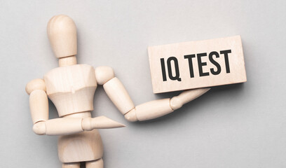 Wooden man shows with a hand to white board with text iq test,concept