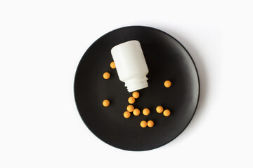 Yellow vitamins pills on a black plate on a white isolated background. Breakfast pills.